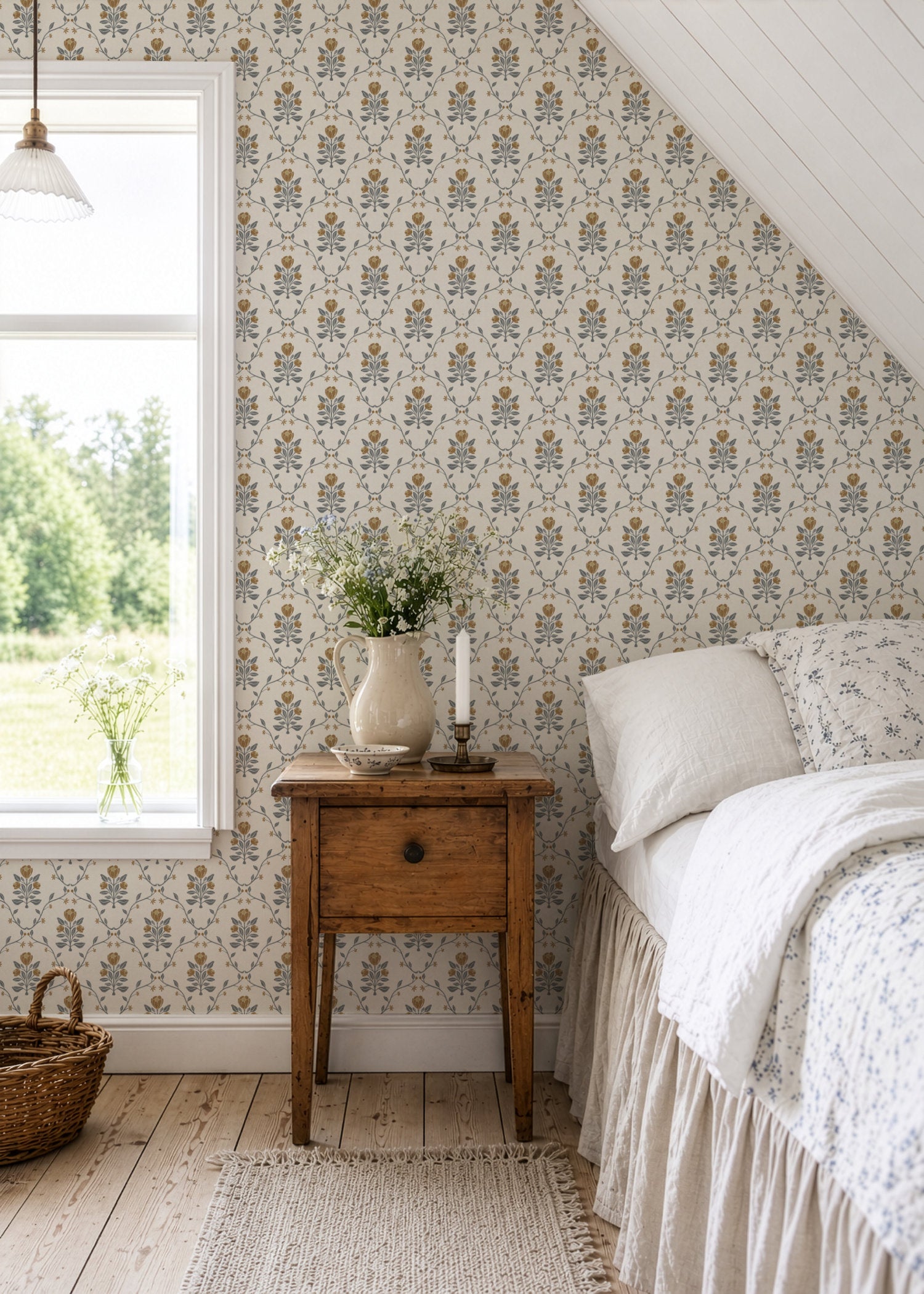 A cozy bedroom corner featuring a tulip trellis wallpaper, a rustic wooden nightstand with a vase of greenery, a bed with white ruffled bedding, and a bright window.