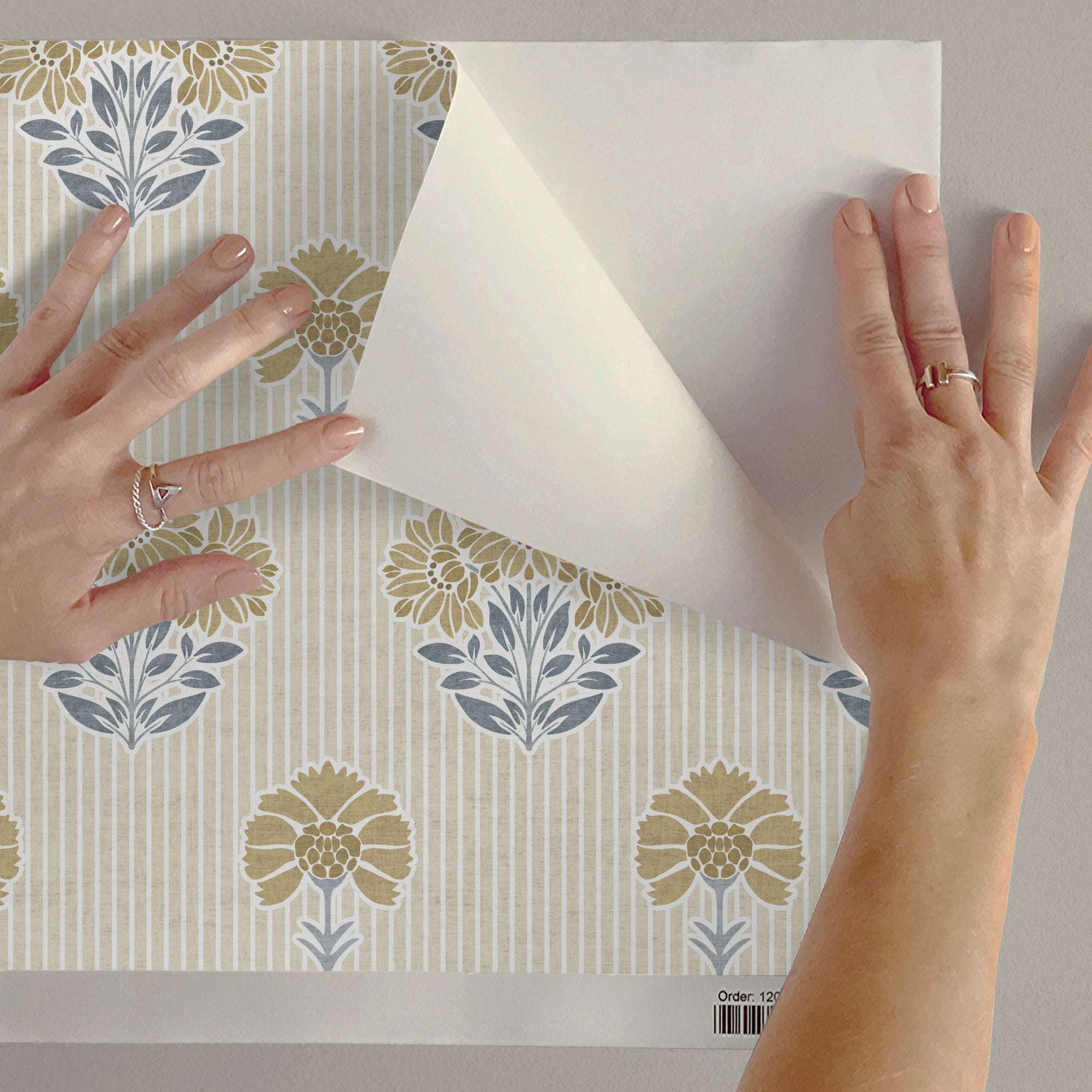 Floral wallpaper sample held by hands showing cream backing and yellow/blue flower print