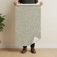 Person holding botanical print wallpaper roll in sage green showing pattern scale