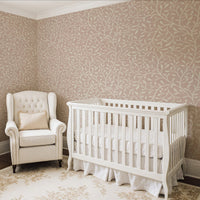 Botanical leaf wallpaper in warm beige in nursery with white cot and armchair