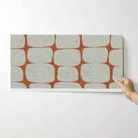 Hand holding a sample of retro geometric stripe wallpaper in terracotta and cream.