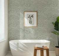 Bathroom with a green coastal waves patterned wallpaper, white freestanding bathtub, wooden stool, and plant.