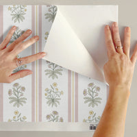 Hands applying peel-and-stick blue and yellow floral striped wallpaper