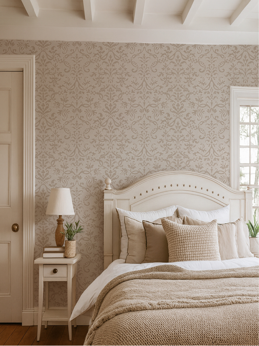 Bedroom with neutral Victorian floral damask wallpaper behind cream bed frame and layered neutral bedding.
