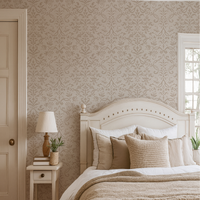 Bedroom with neutral Victorian floral damask wallpaper behind cream bed frame and layered neutral bedding.